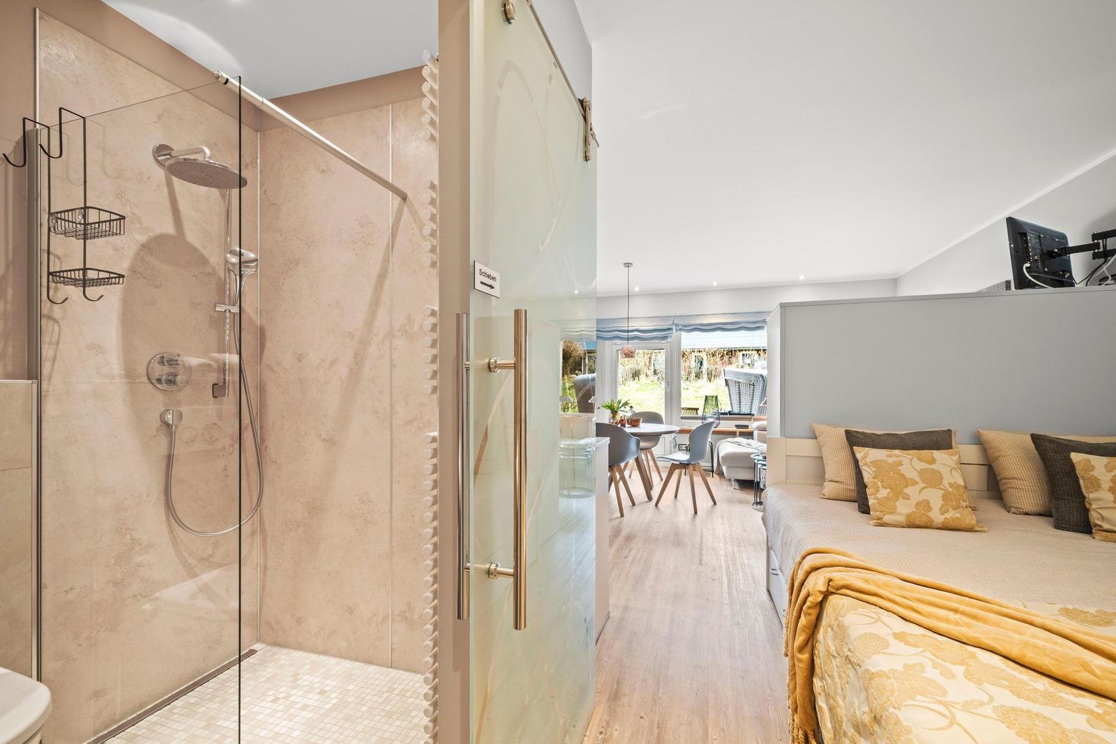 Dusche mit Glaswand, Schlafzimmer mit Bett und TV, Essbereich mit Tisch und Stühlen.