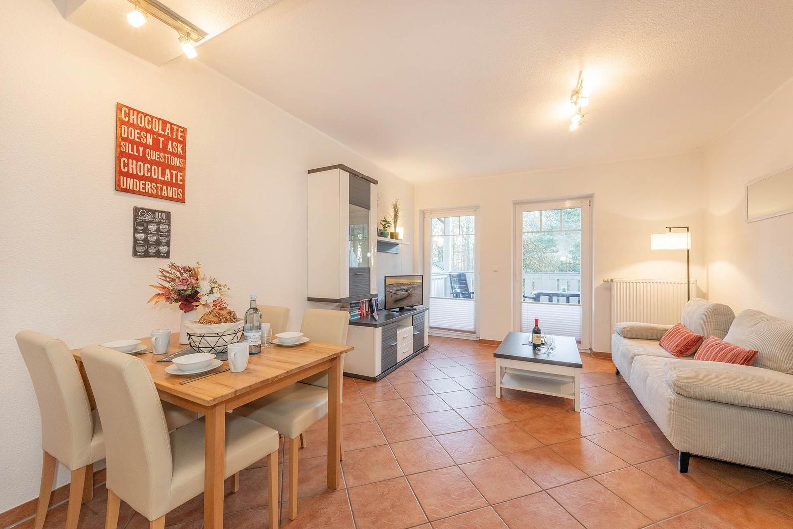 Wohn- und Essbereich mit Sofa, Esstisch und TV. Terrasse über Glastüren erreichbar.