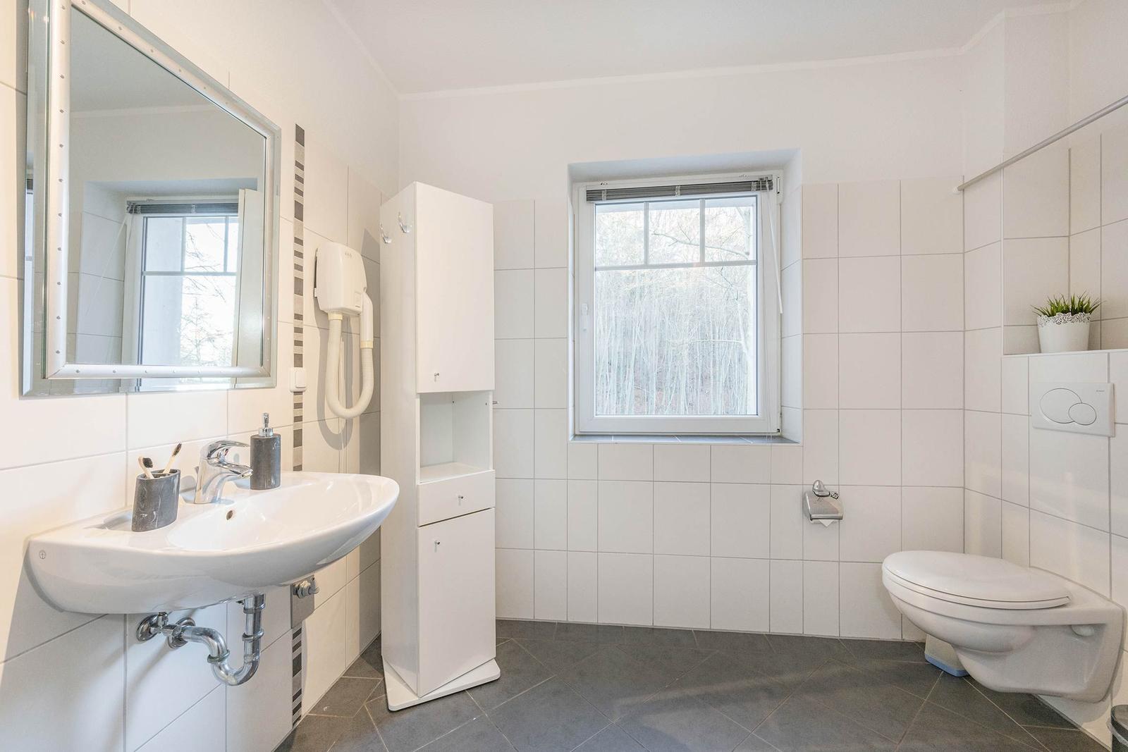 Badezimmer mit Waschbecken, Spiegel, Toilette und Fenster.