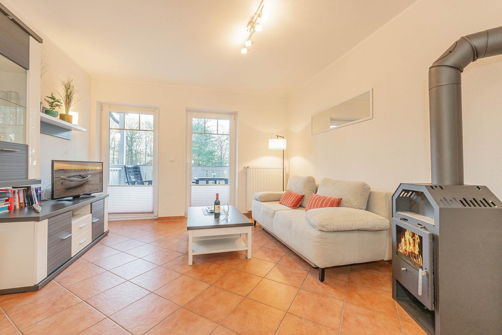 Wohnzimmer mit Sofa, Kaminofen und TV. Terrasse über Fenster sichtbar.