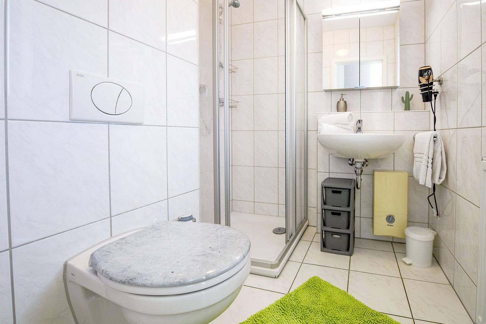 Badezimmer mit Dusche, Waschbecken und Toilette. Grün Teppich und Handtuchhalter.