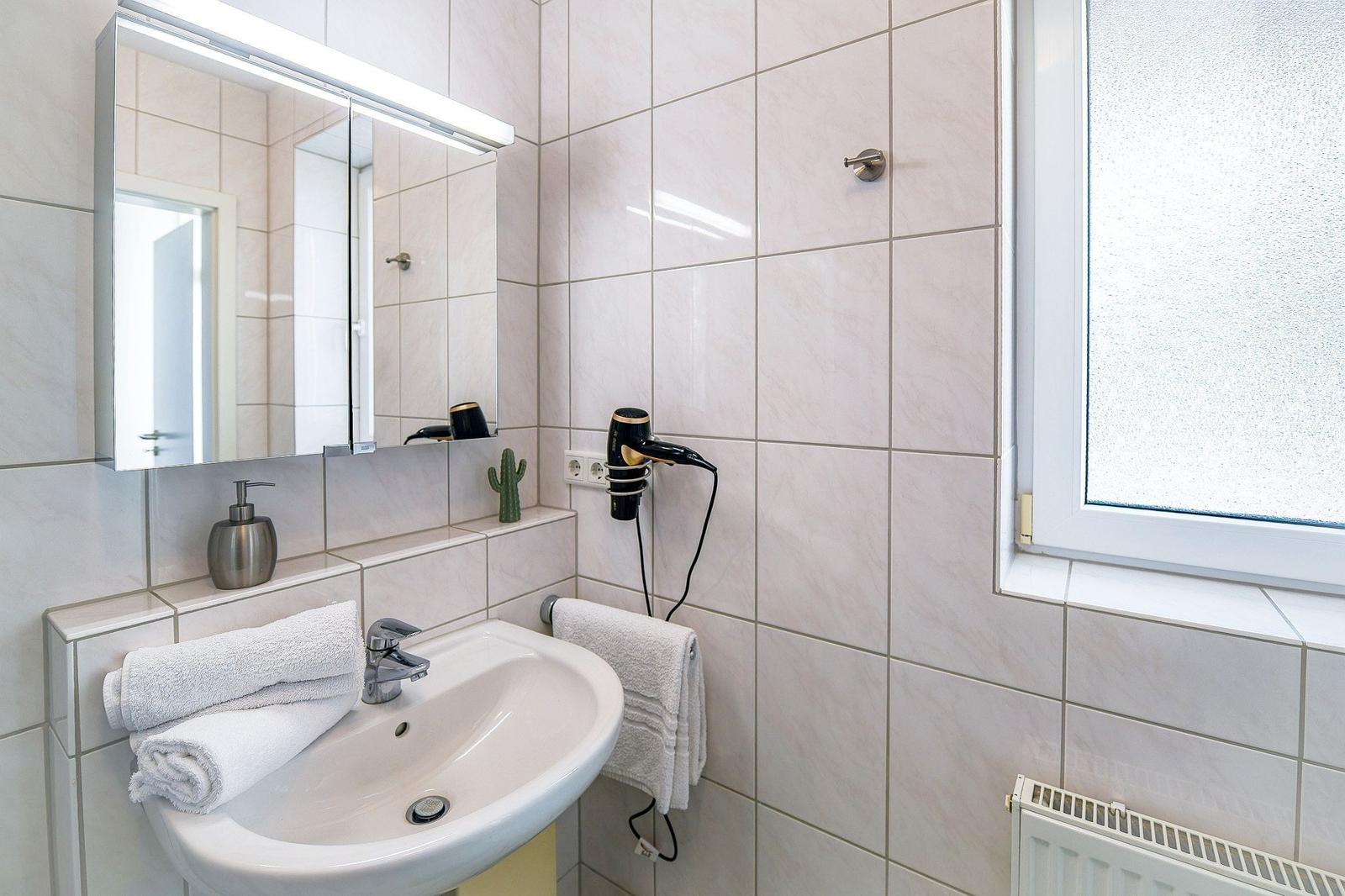 Badezimmer mit Waschbecken, Spiegel, Handtuch und Fenster.