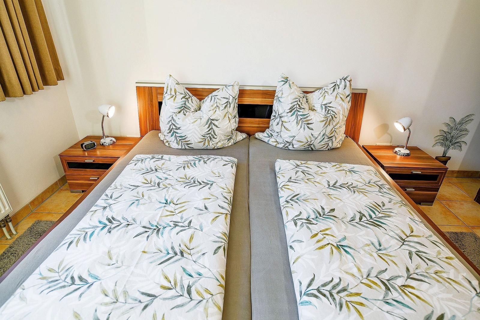 Zwei Betten mit Blattmuster-Bettwäsche, Nachttische mit Lampen und Pflanze.
