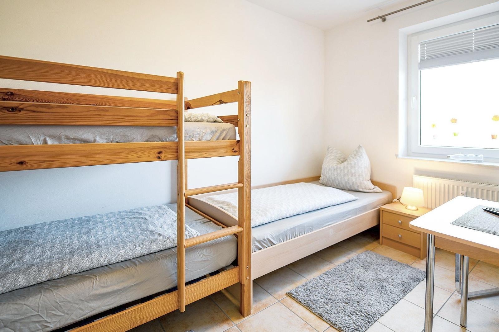 Zimmer mit Doppelstockbett, Schreibtisch und Fenster mit Jalousie.