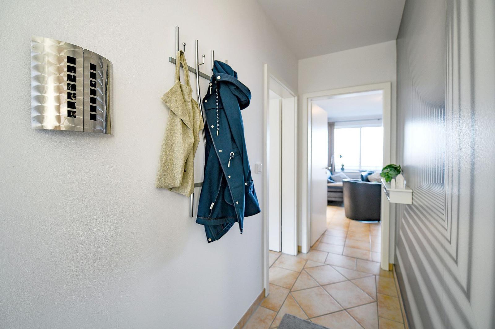 Flur mit Garderobe, Jacken und Blick in Wohnzimmer mit Sofa und Fenster.