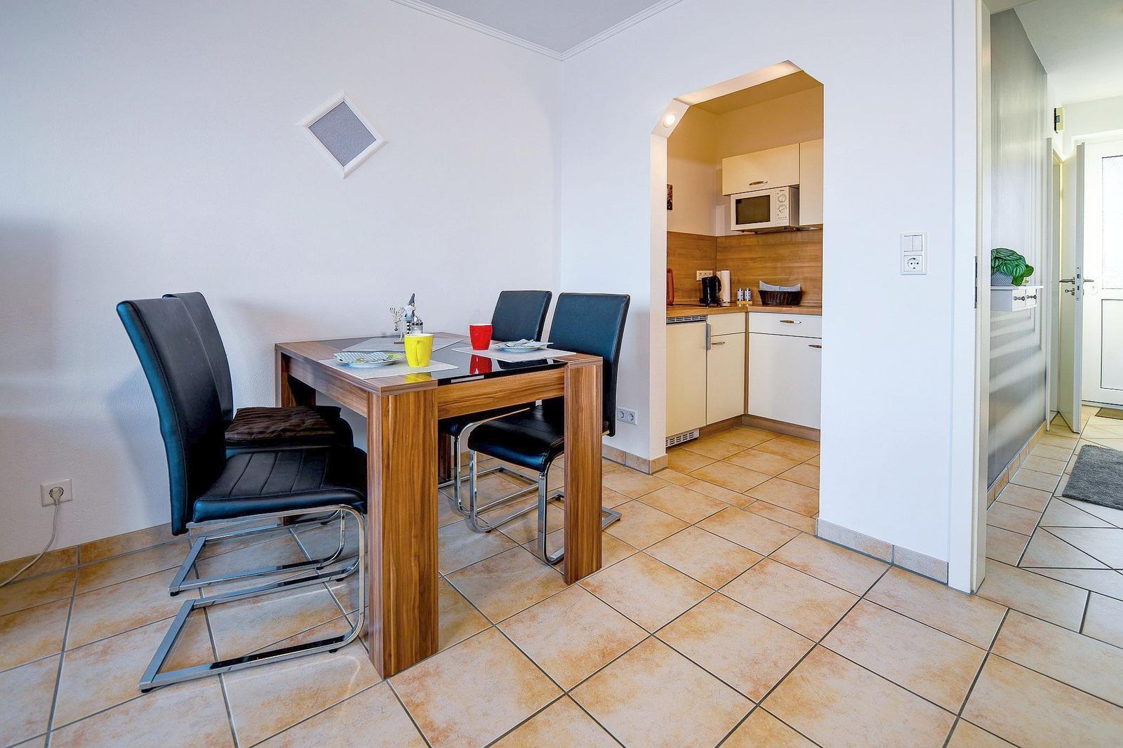 Essbereich mit Tisch und Stühlen, Küche im Hintergrund, Fliesenboden und Wanddekoration.