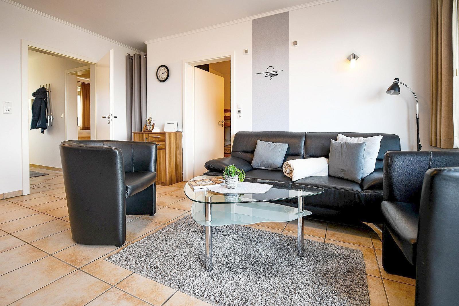 Wohnzimmer mit Ledersofa, Glas-Tisch und Teppich auf Fliesenboden.