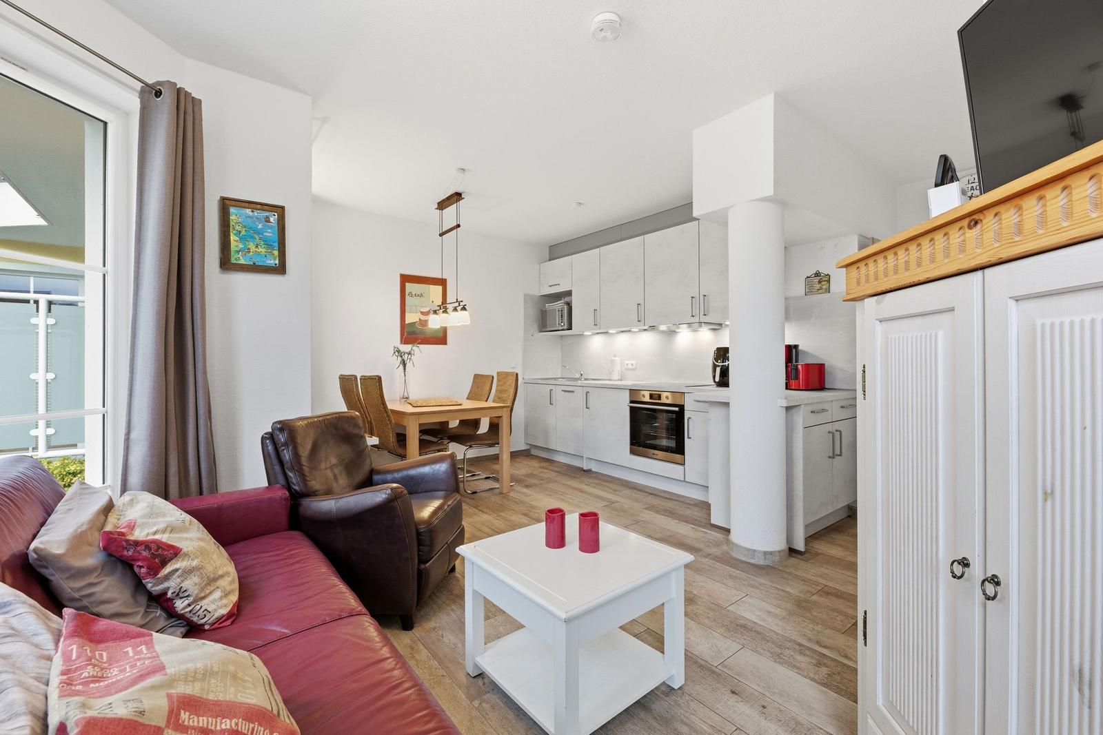 Wohnbereich mit Küche, Sofa, Esstisch und TV. Holzboden und weiße Möbel.