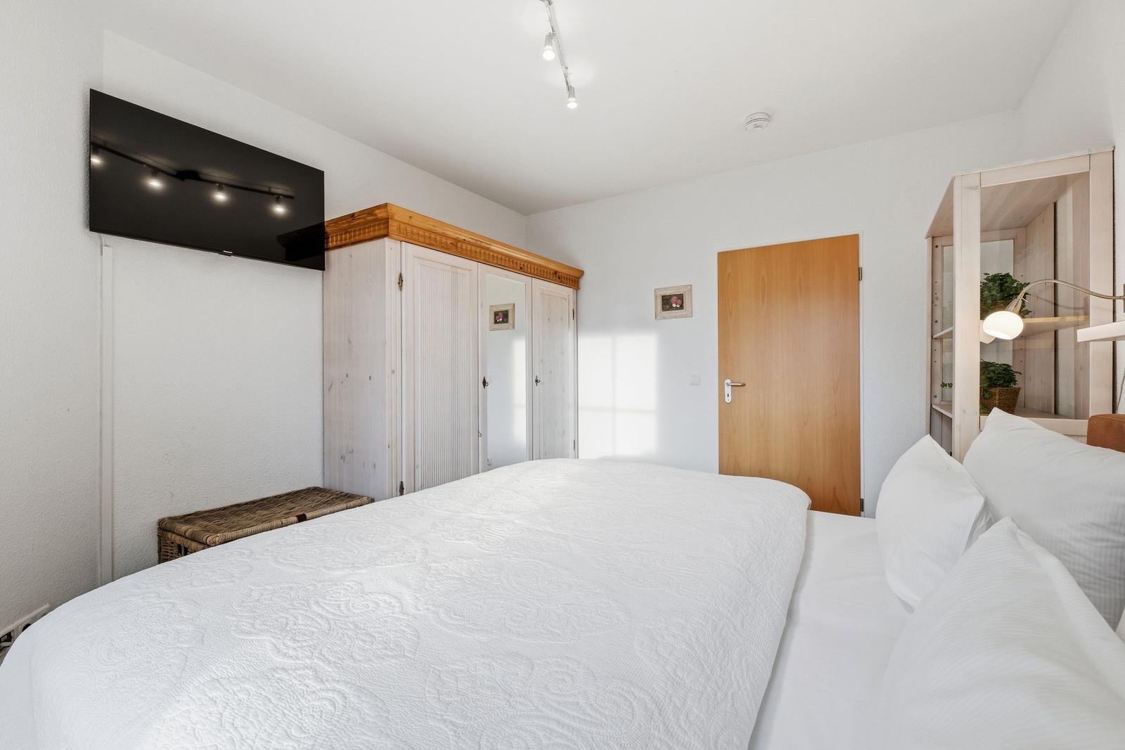 Schlafzimmer mit Bett, Kleiderschrank und Fernseher an der Wand.