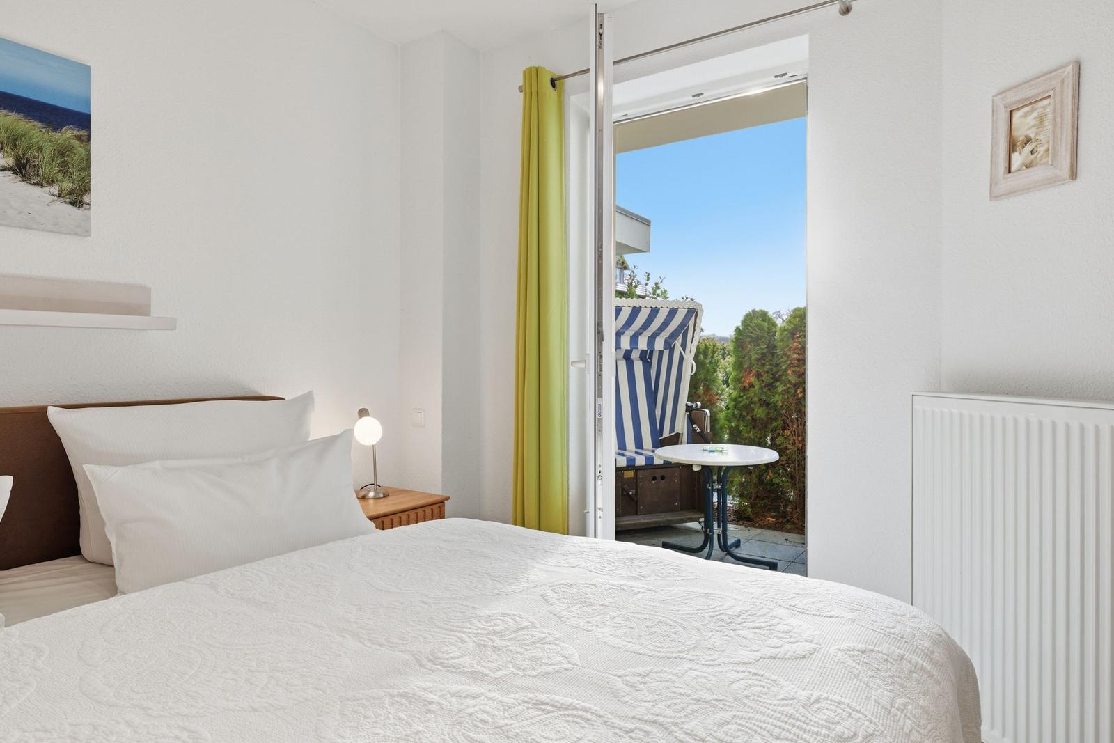 Schlafzimmer mit Blick auf Balkon mit Strandkorb und Tisch.