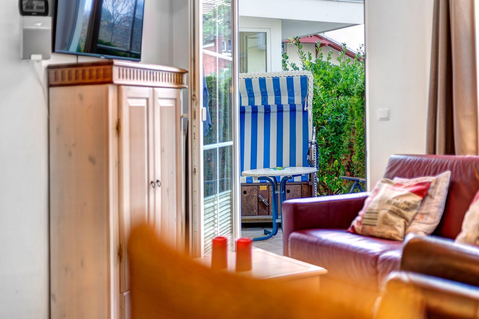Wohnzimmer mit Sofa und Blick auf Terrasse mit Strandkorb.