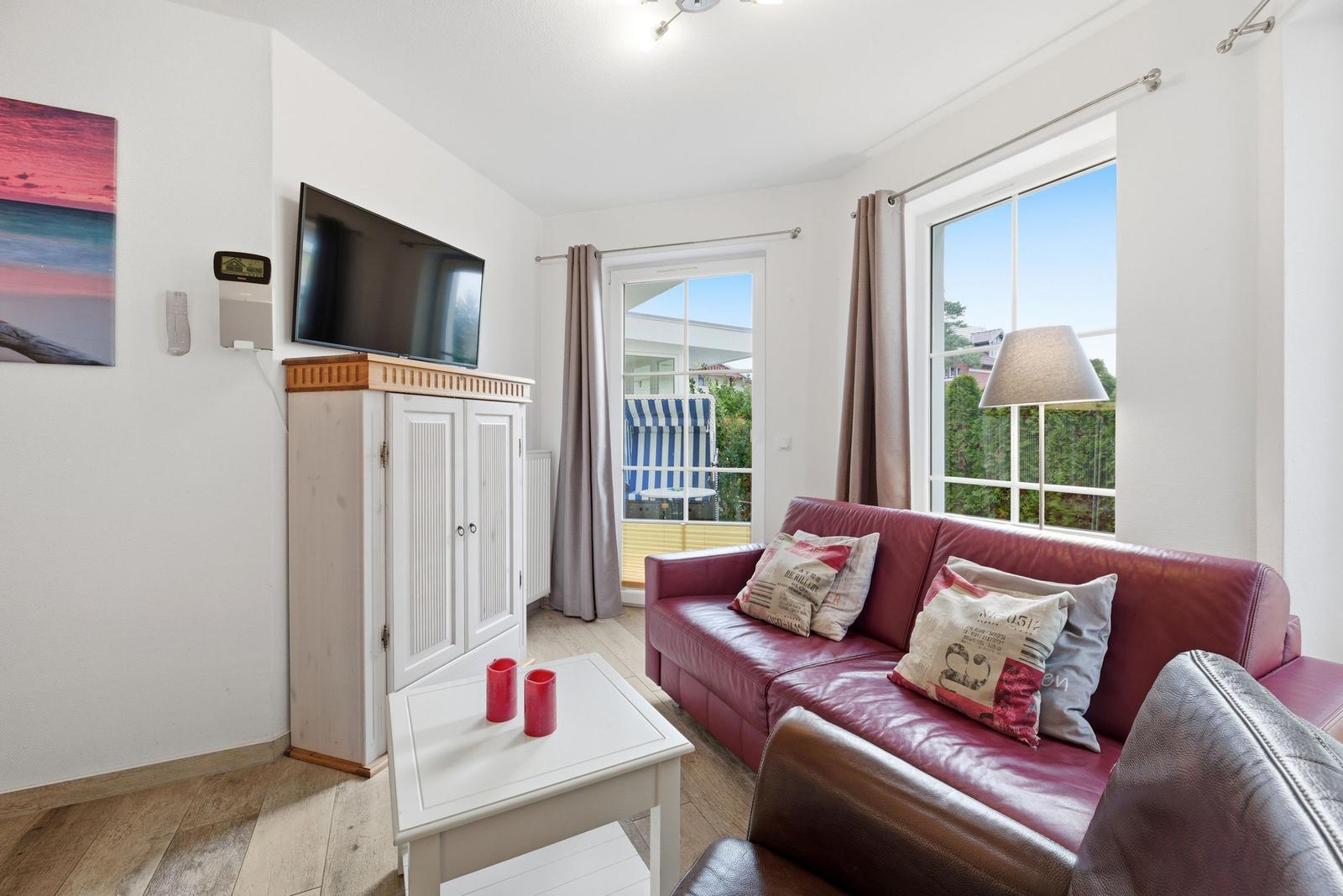 Wohnzimmer mit rotem Sofa, Fernseher und Fenster zur Terrasse.