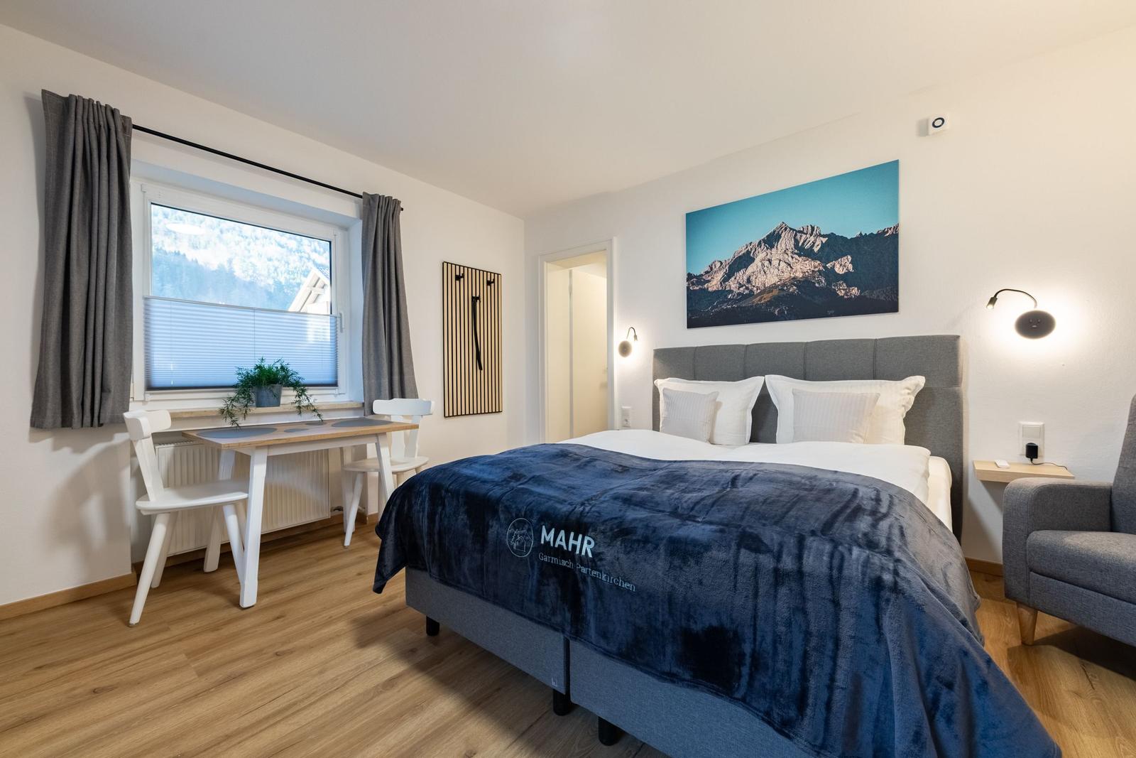 Schlafzimmer mit Bett, Schreibtisch und Fensterblick auf Berge.