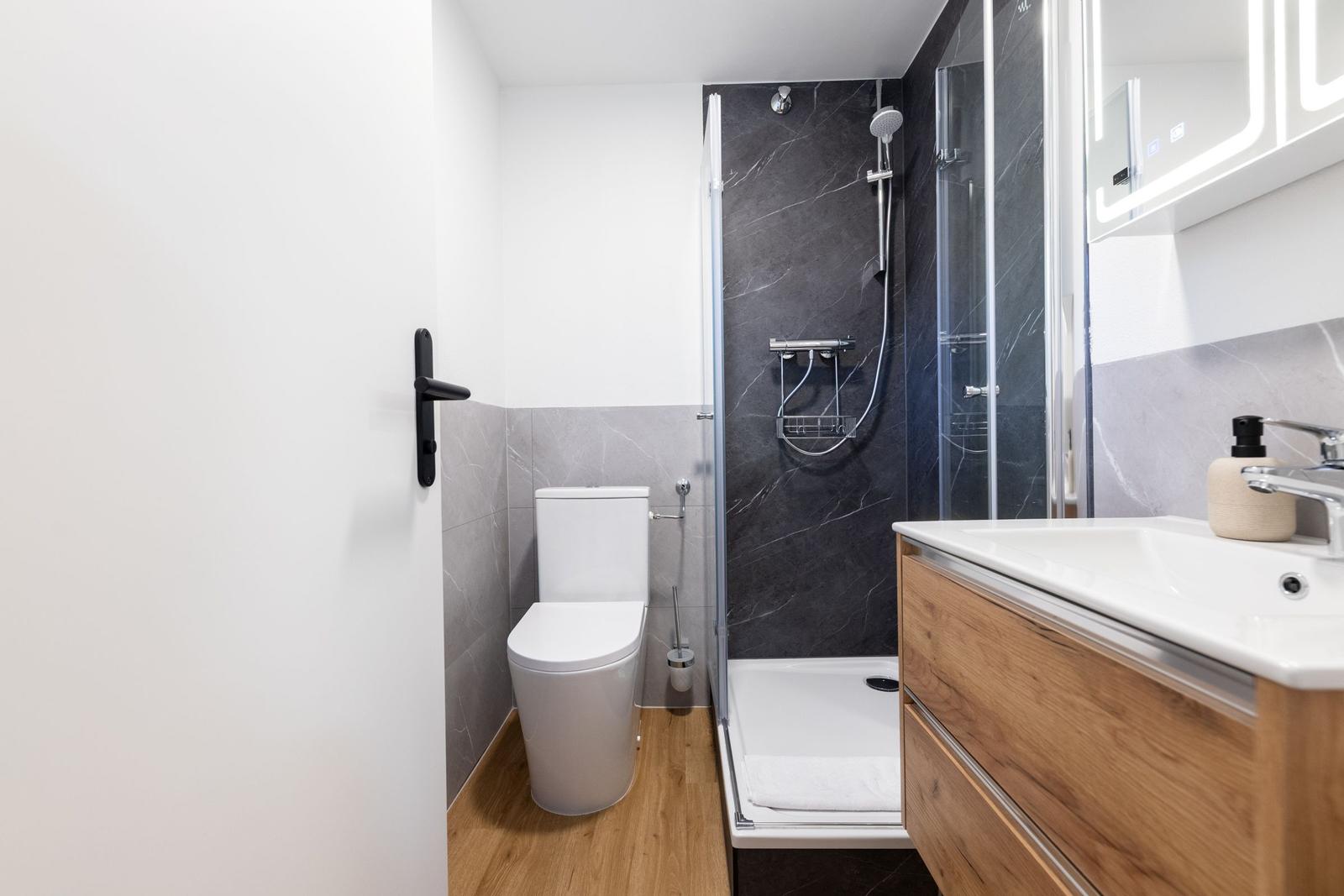 Badezimmer mit Dusche, Toilette und Waschbecken mit Holzschrank.