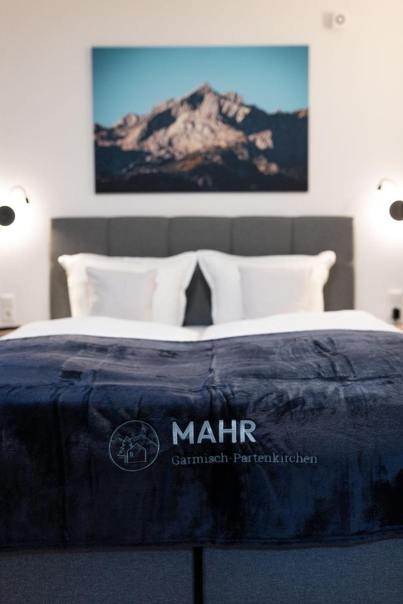 Doppelbett mit dunkelblauer Bettdecke und Bergbild an der Wand.