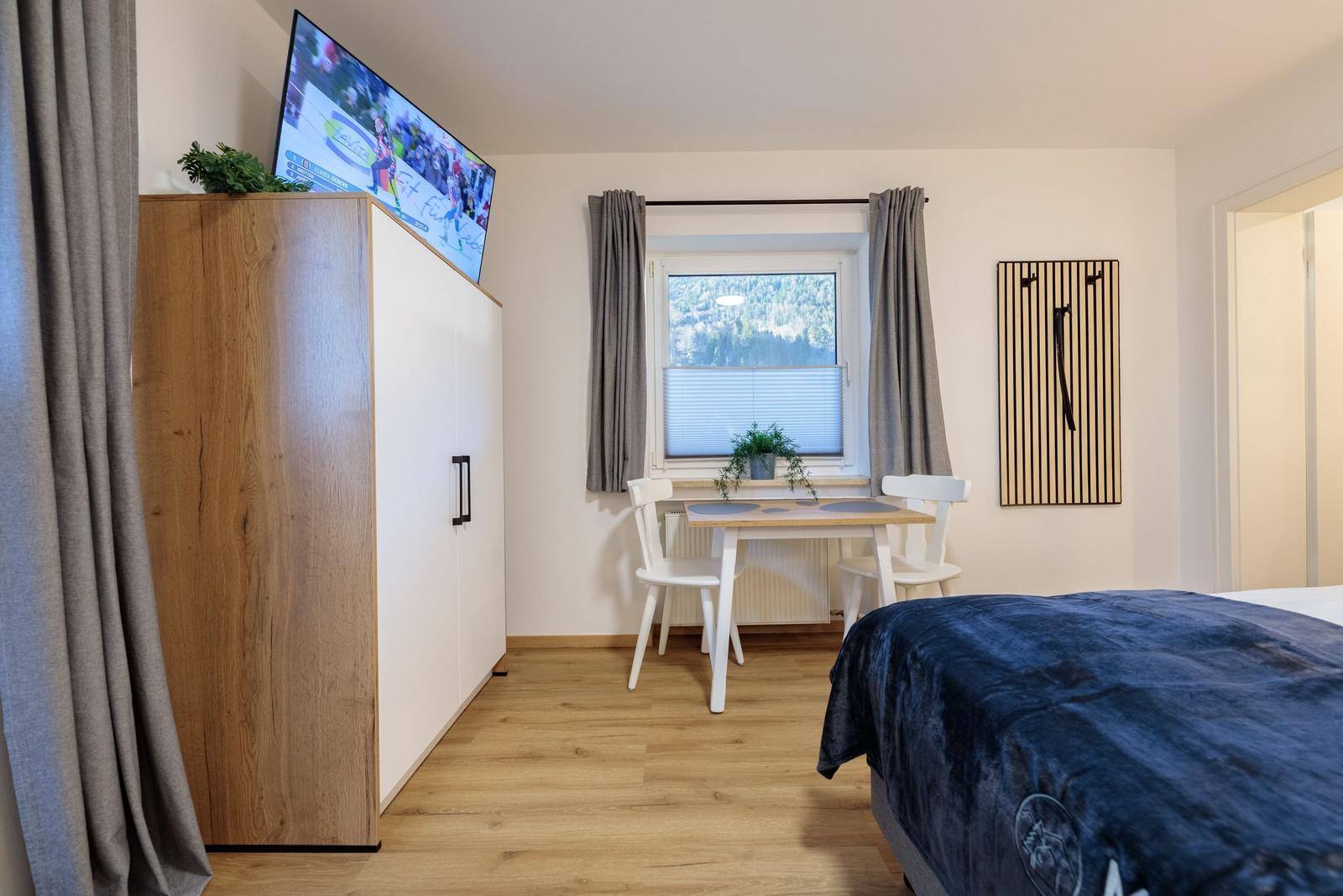 Zimmer mit Bett, Schreibtisch, TV und Fenster mit Bergblick.