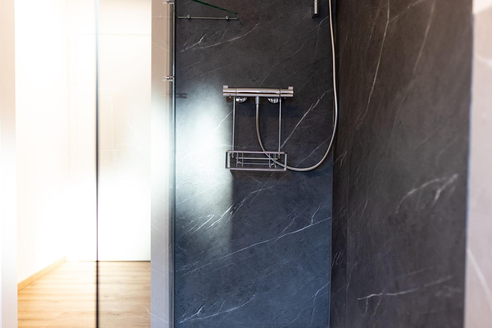 Duschkabine mit dunklem Marmor und chromfarbenem Duschset.