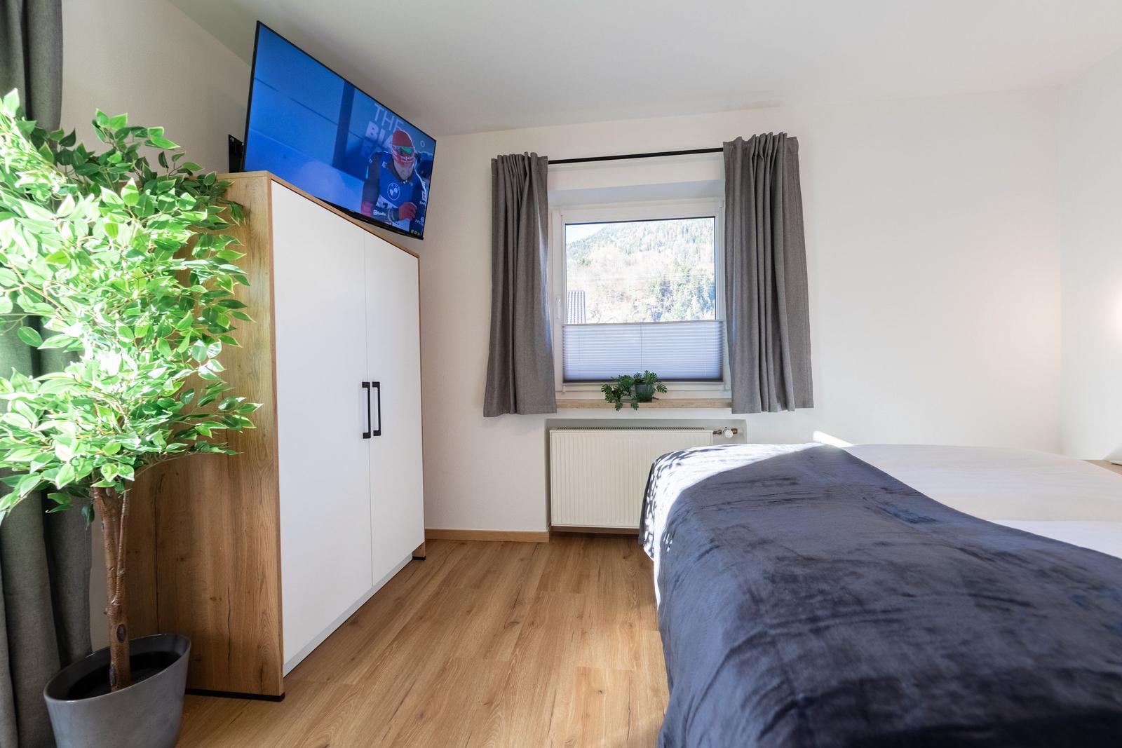 Schlafzimmer mit Bett, Kleiderschrank und Fenster mit Bergblick.