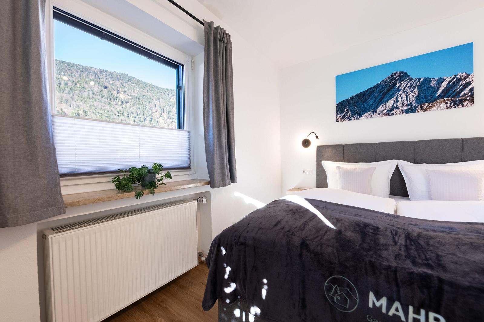 Schlafzimmer mit Bett, Fenster und Wandbild. Blick auf bewaldete Berge.