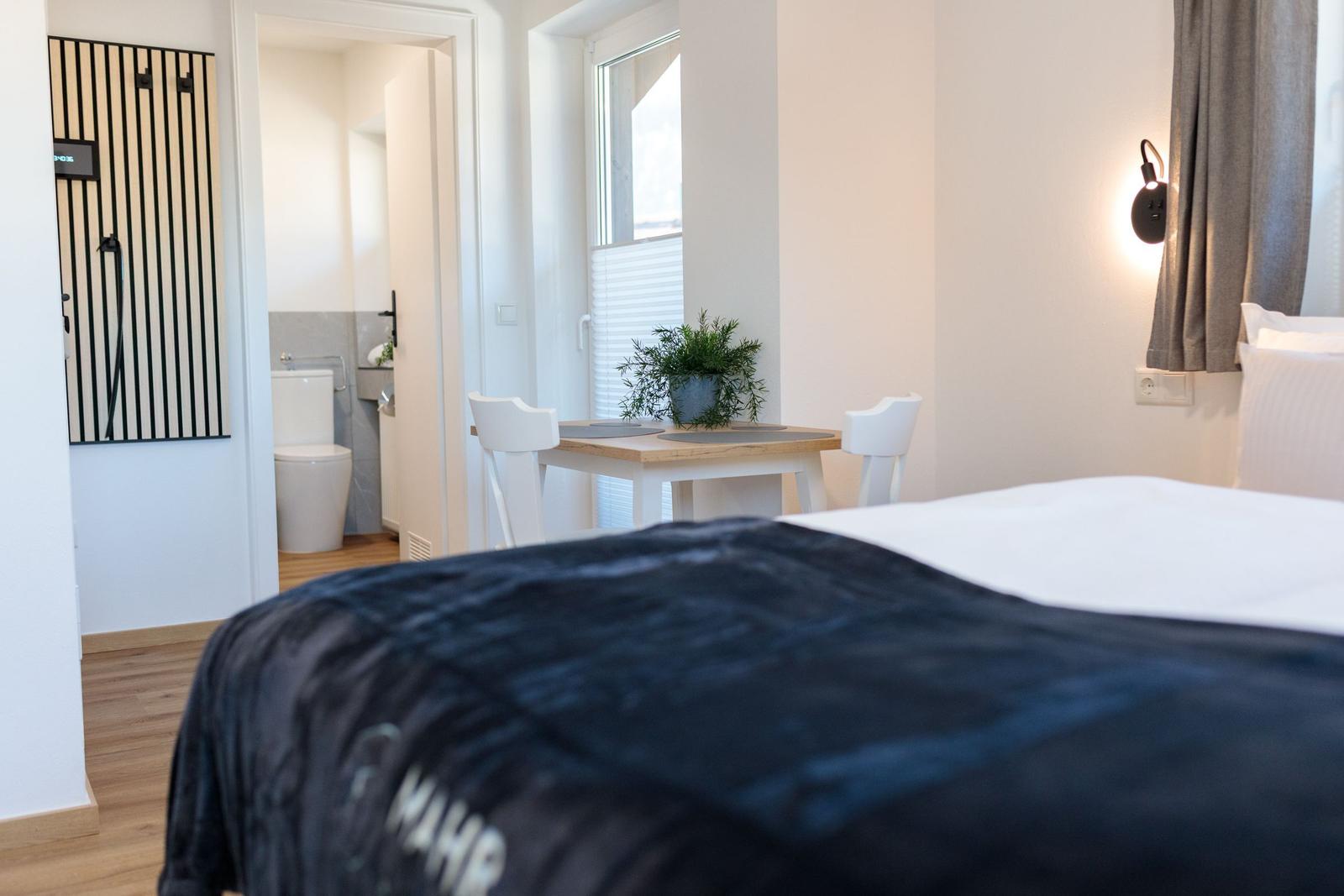 Schlafzimmer mit Bett, Tisch und Stühlen. Im Hintergrund ist die Toilette sichtbar.