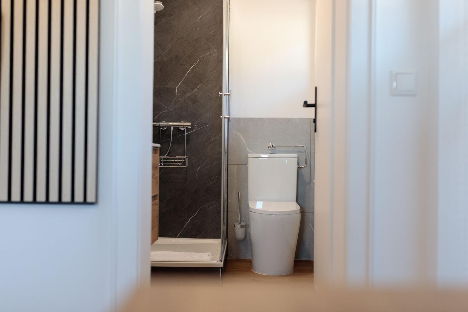 Badezimmer mit Dusche und Toilette. Marmorwände und Holzboden.