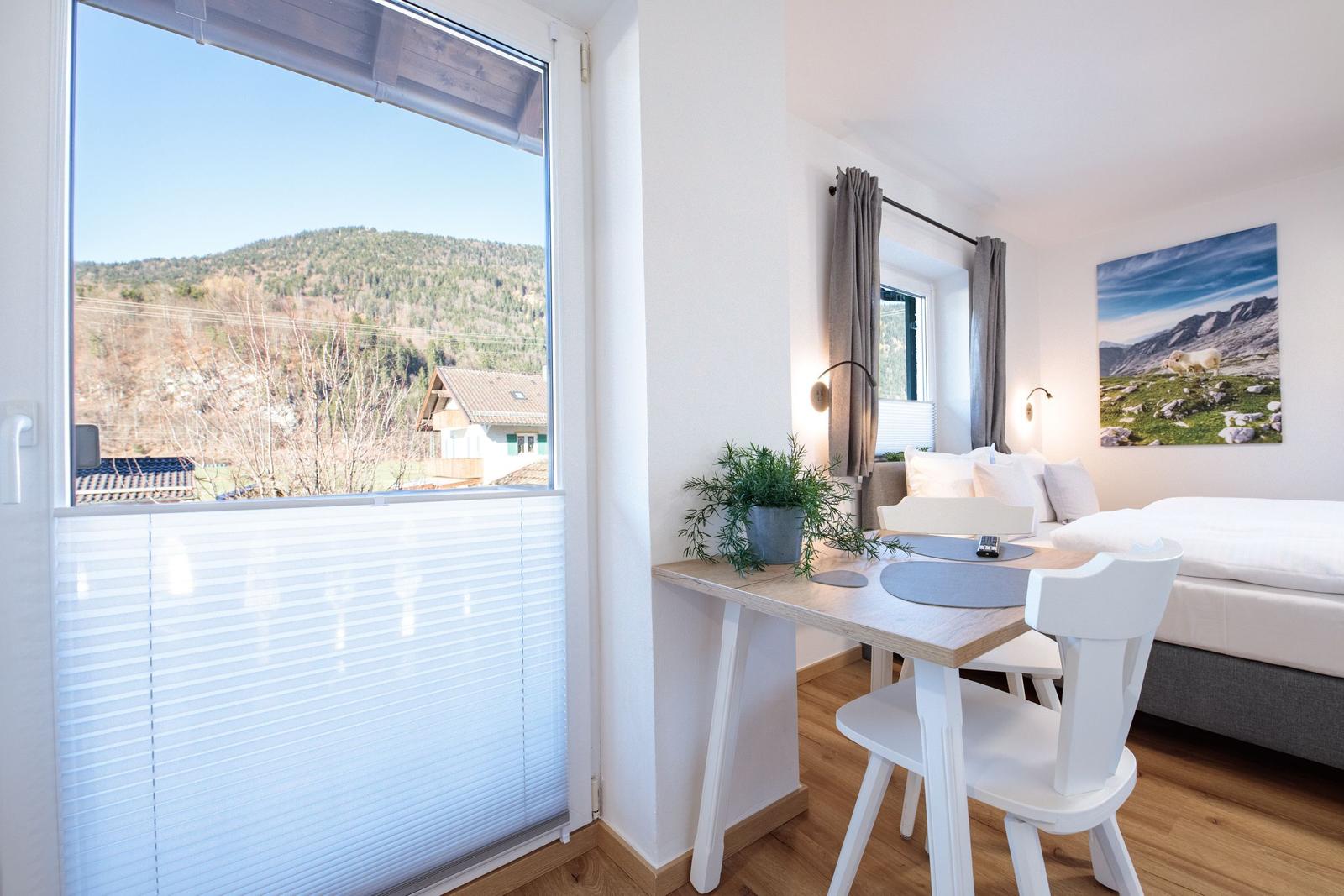 Zimmer mit Blick auf Hügel, Tisch mit Stühlen, Bett und Wandbild.