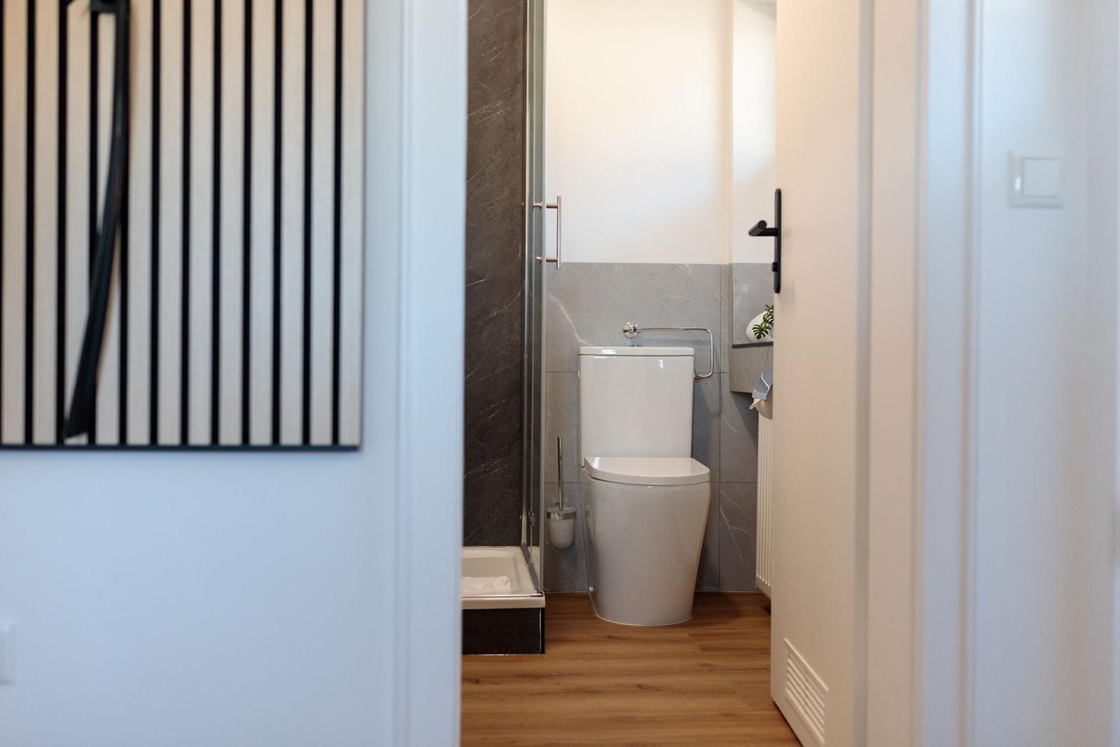 Badezimmer mit Toilette und Dusche, Holzboden und grauen Fliesen