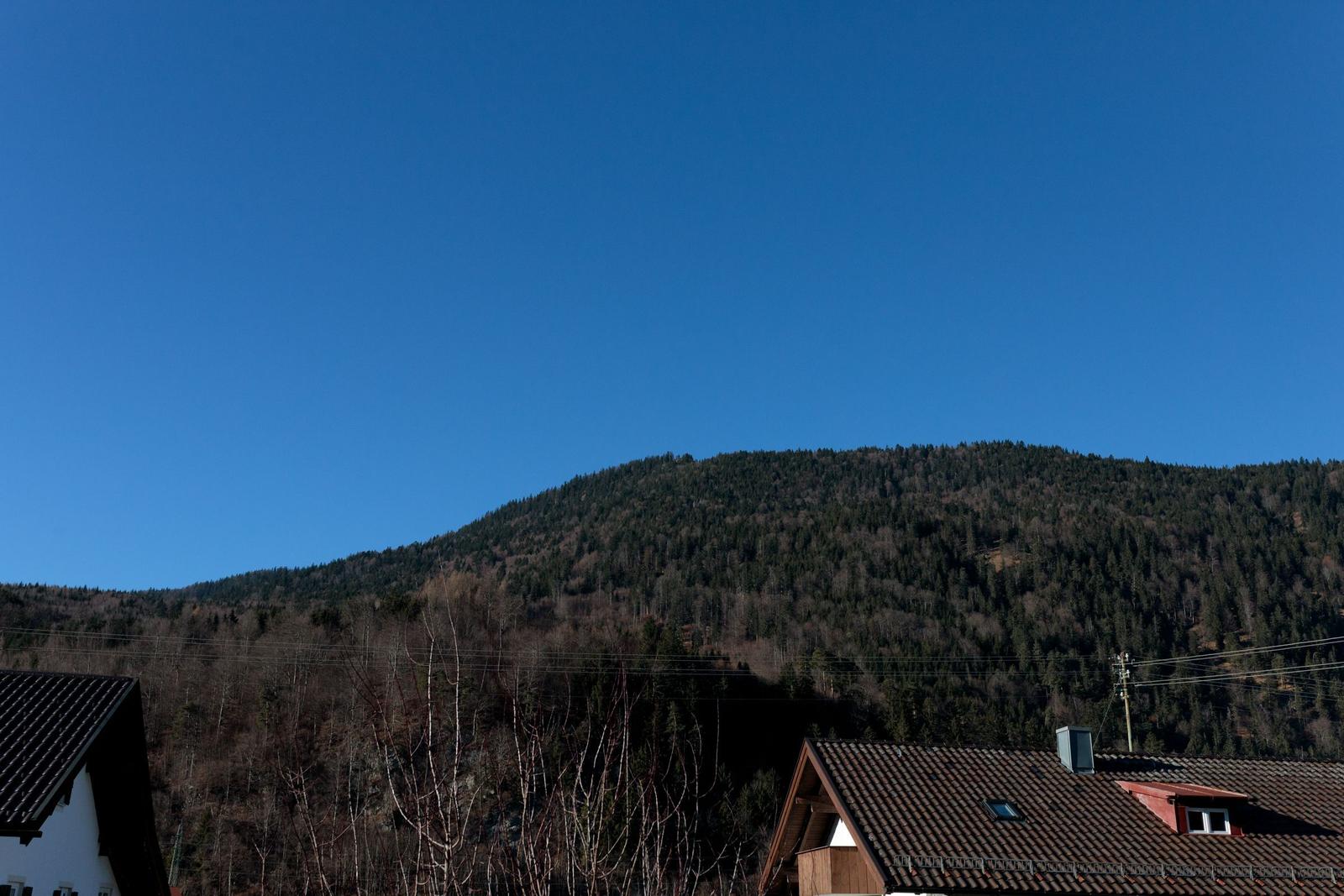 Haus mit Dach und Blick auf bewaldeten Berg unter blauem Himmel.