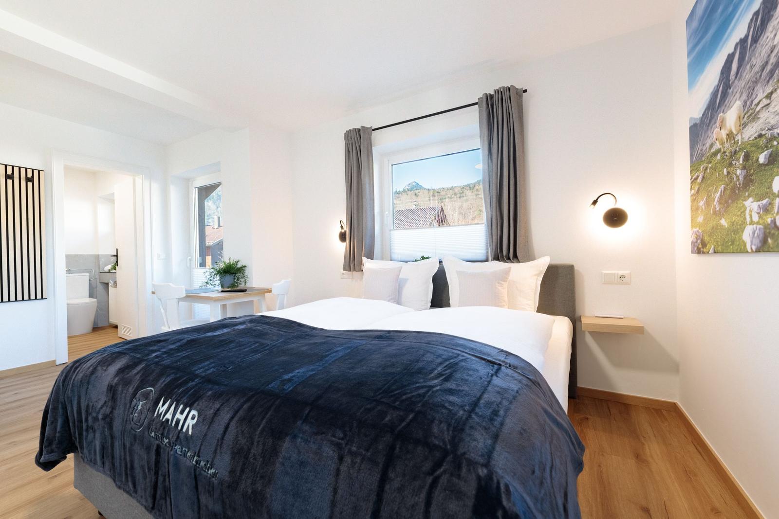 Schlafzimmer mit Doppelbett, Fensterblick und Wandbild. Nebenraum mit Toilette und Tisch.