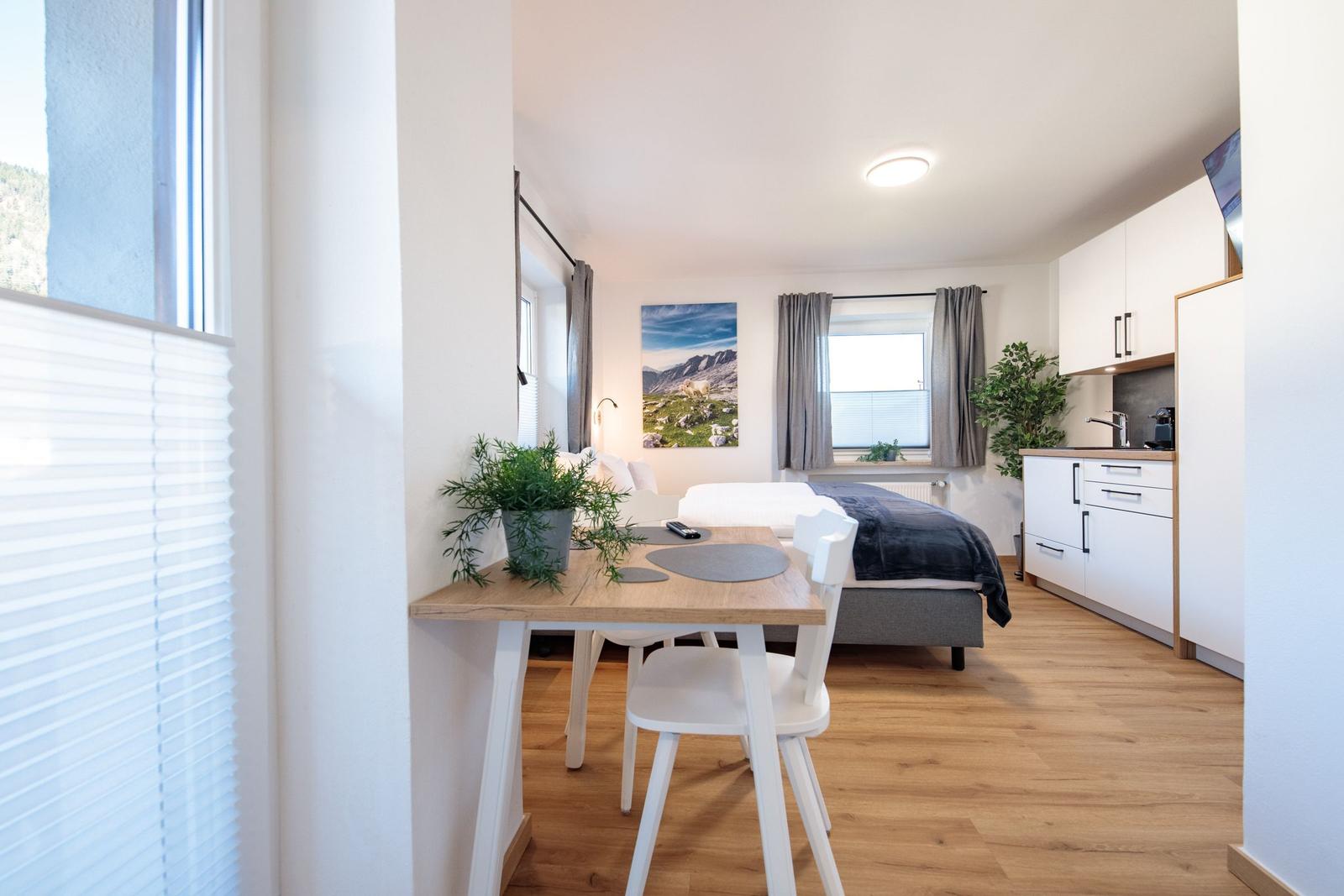 Schlafzimmer mit Essbereich und kleiner Küche. Holzboden und Fenster mit Jalousien.