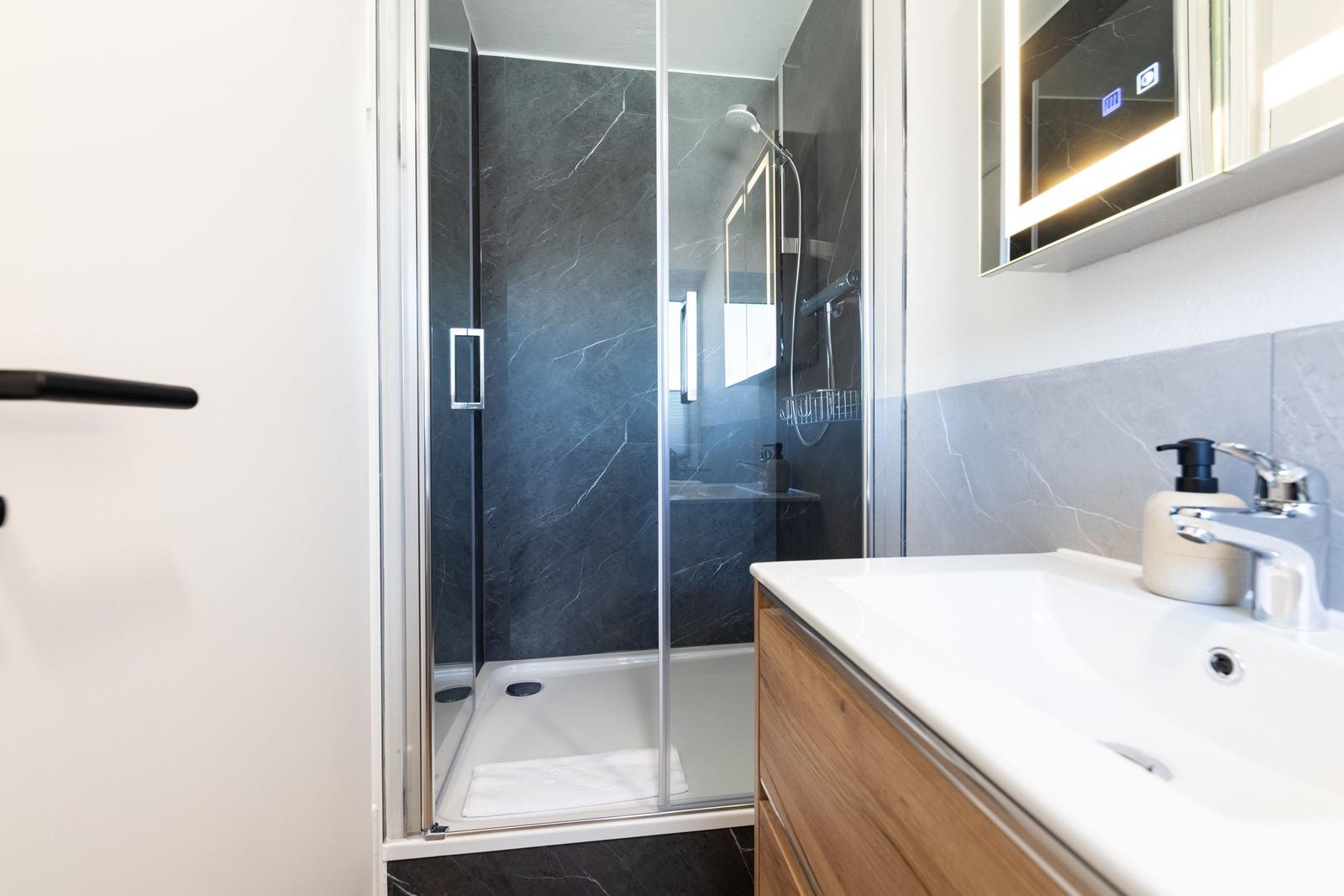 Bad mit Dusche, Waschbecken und beleuchtetem Spiegel