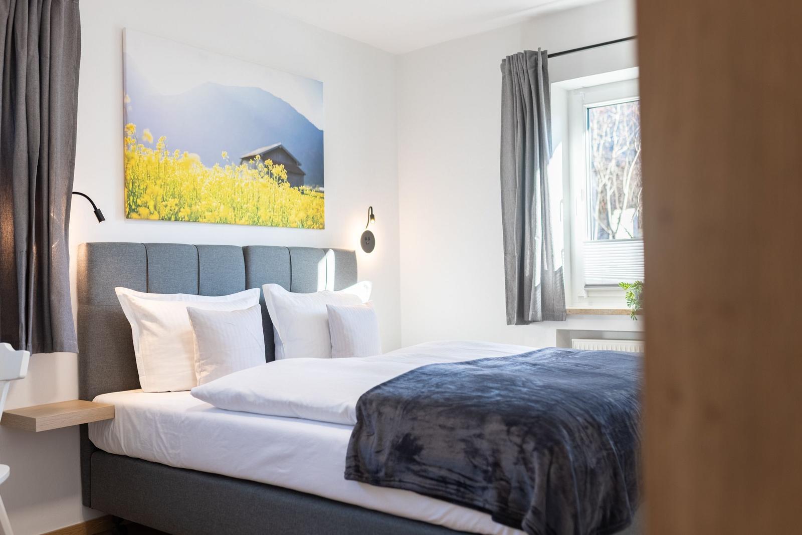 Schlafzimmer mit Bett, Wandbild und Fenster mit Blick auf Bäume.