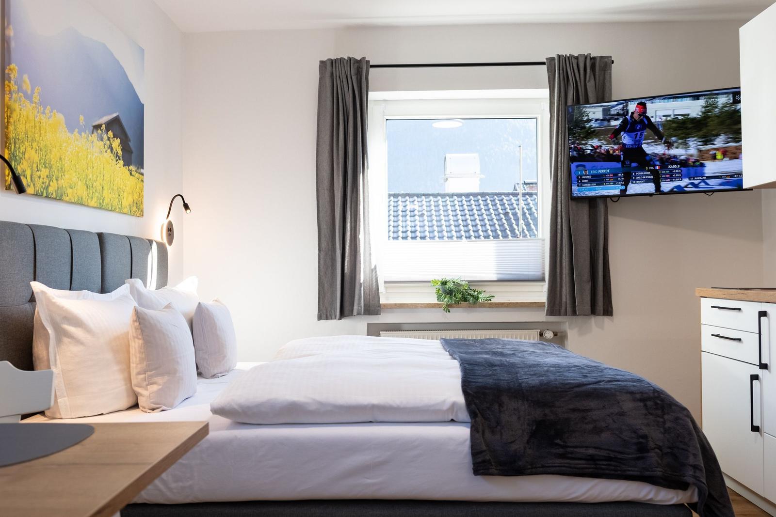 Schlafzimmer mit Bett, Fenster, TV und Wandbild.