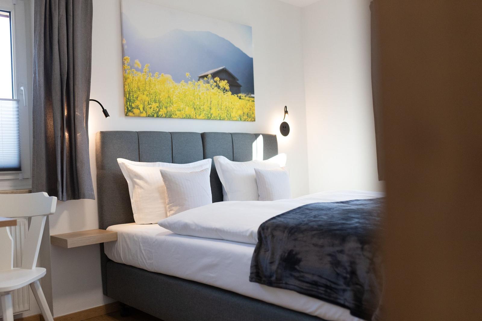 Schlafzimmer mit Bett, Wandbild und Nachttisch. Fenster mit Vorhängen.