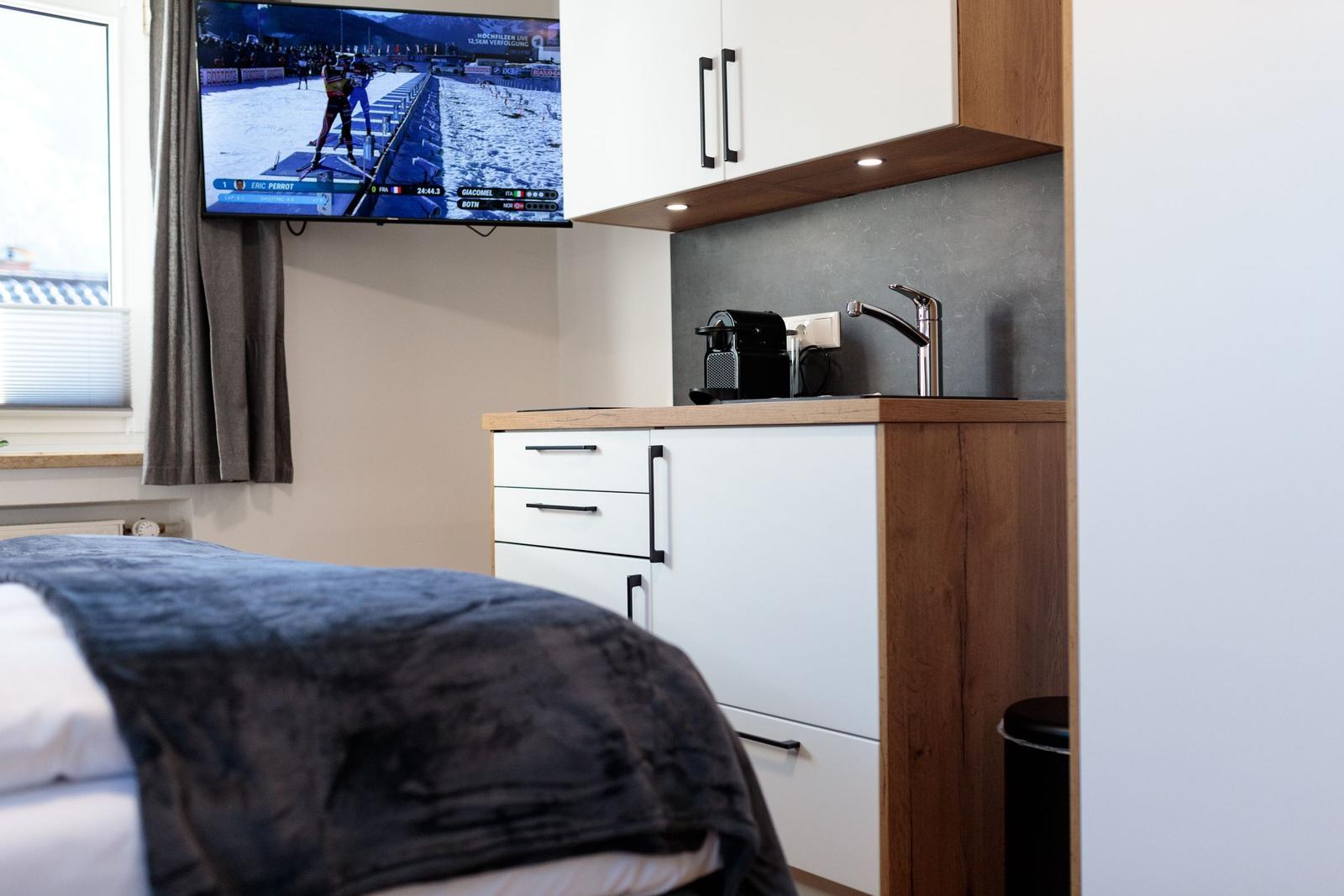 Schlafzimmer mit kleiner Küchenzeile und Fernseher an der Wand.