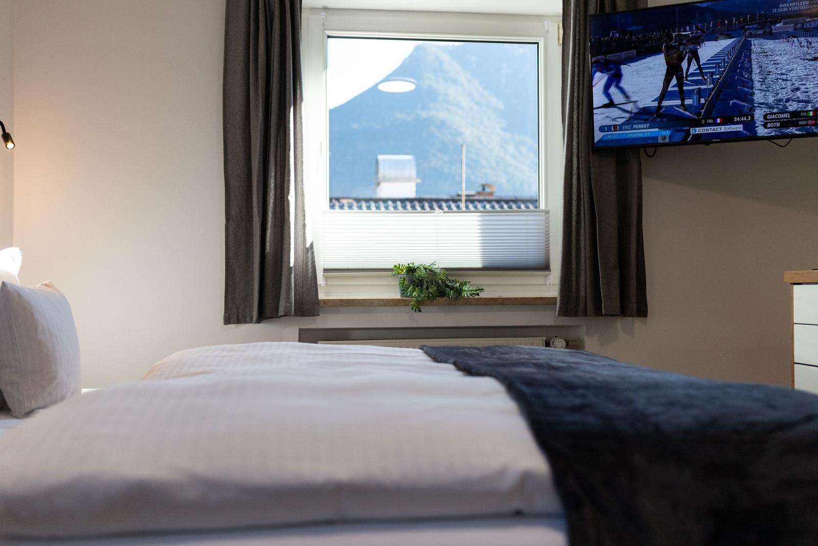 Ein Bett mit Blick auf einen Berg. Ein Fernseher zeigt eine Wintersportveranstaltung.