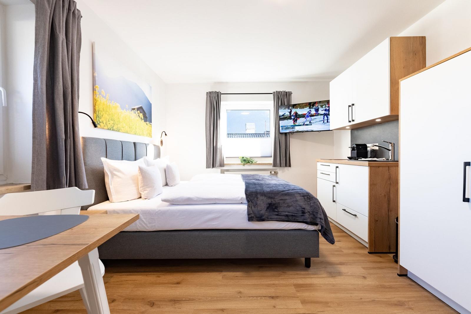 Schlafzimmer mit Bett, Schreibtisch und Küchenzeile. Fernseher an der Wand.