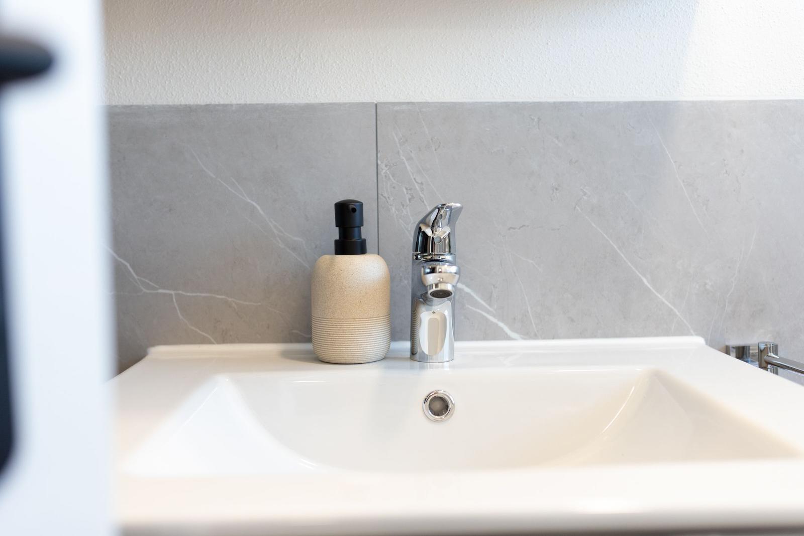 Waschbecken mit Wasserhahn und Seifenspender an grauer Wand