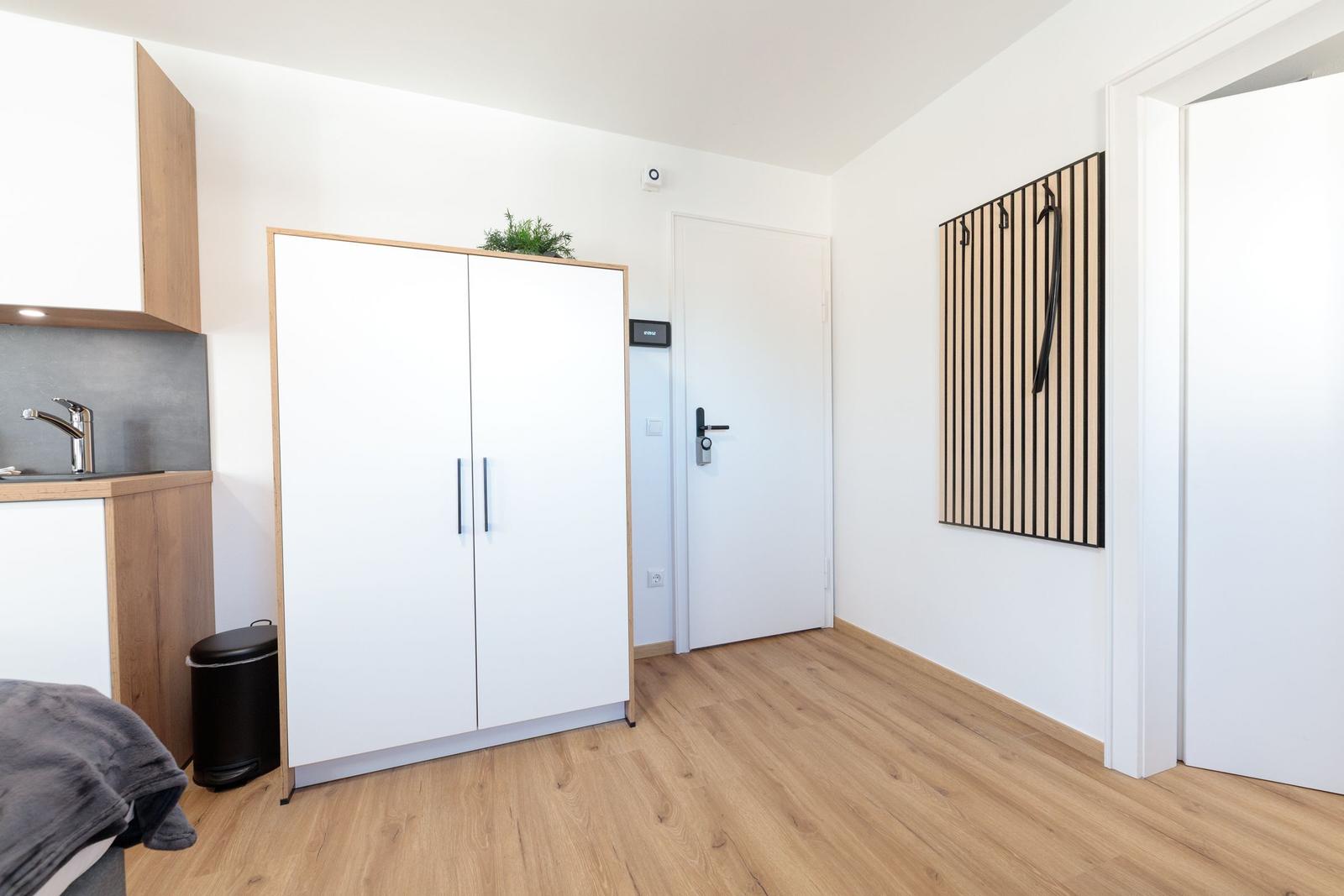 Eingangsbereich mit Kleiderschrank, Küchenzeile und Garderobe an der Wand.