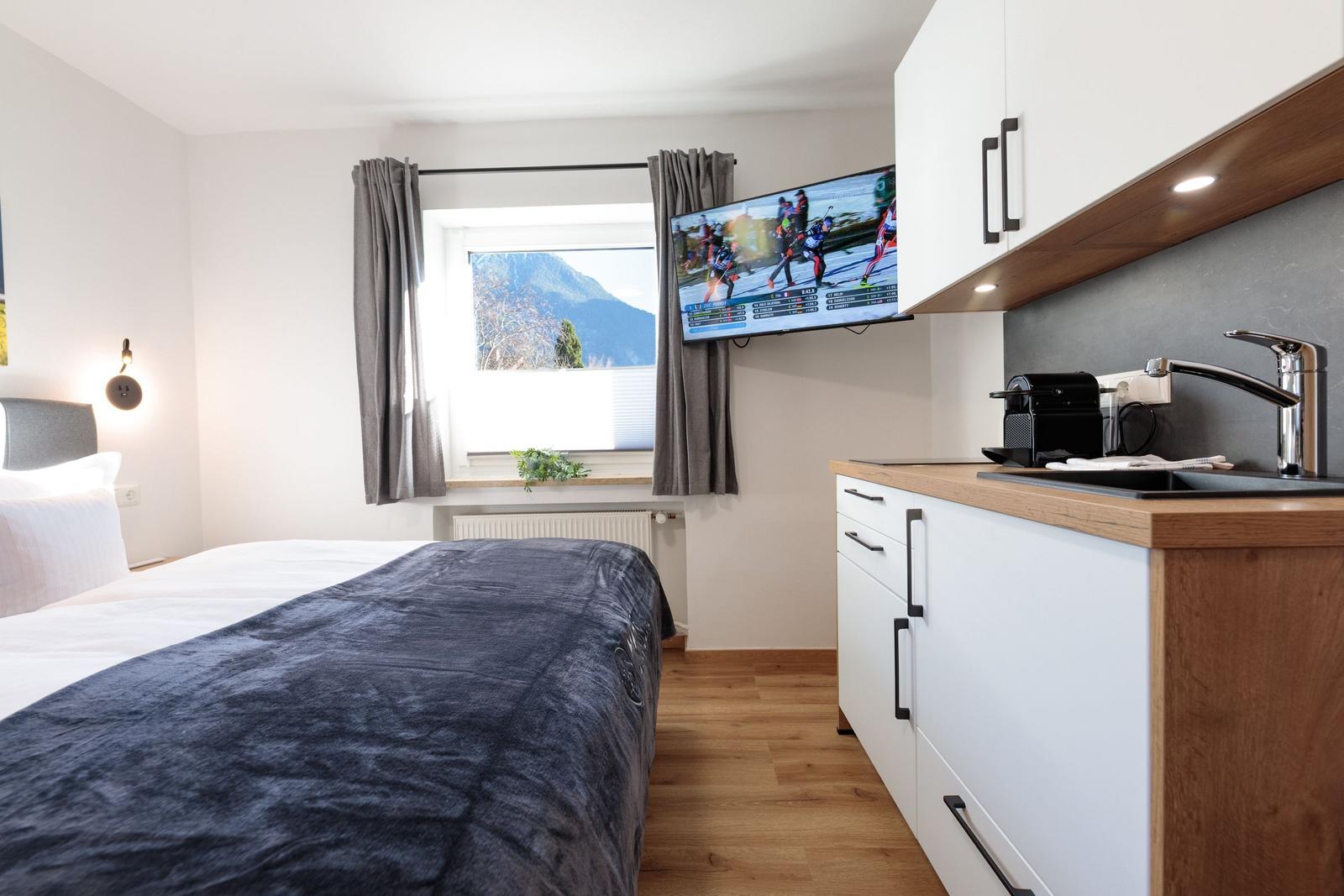 Schlafzimmer mit Bett, Fenster und Küchenzeile mit TV.
