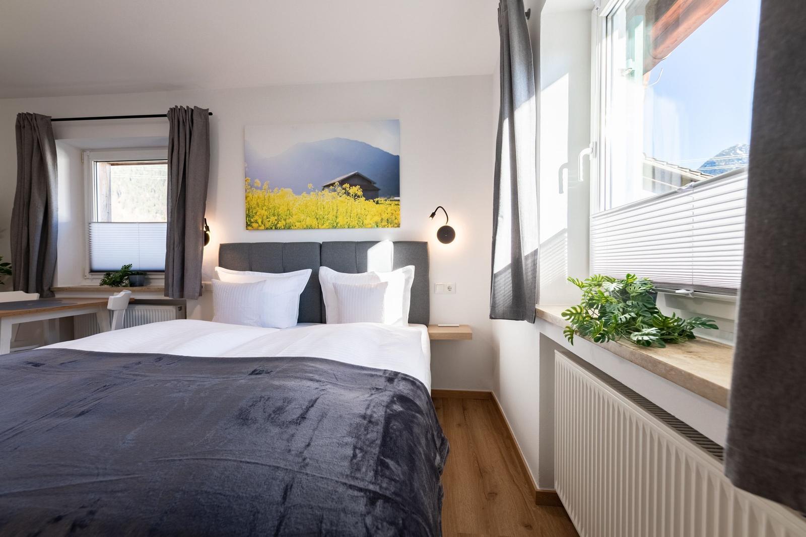 Schlafzimmer mit Bett, Wandbild und Fenstern mit Blick auf Berge.