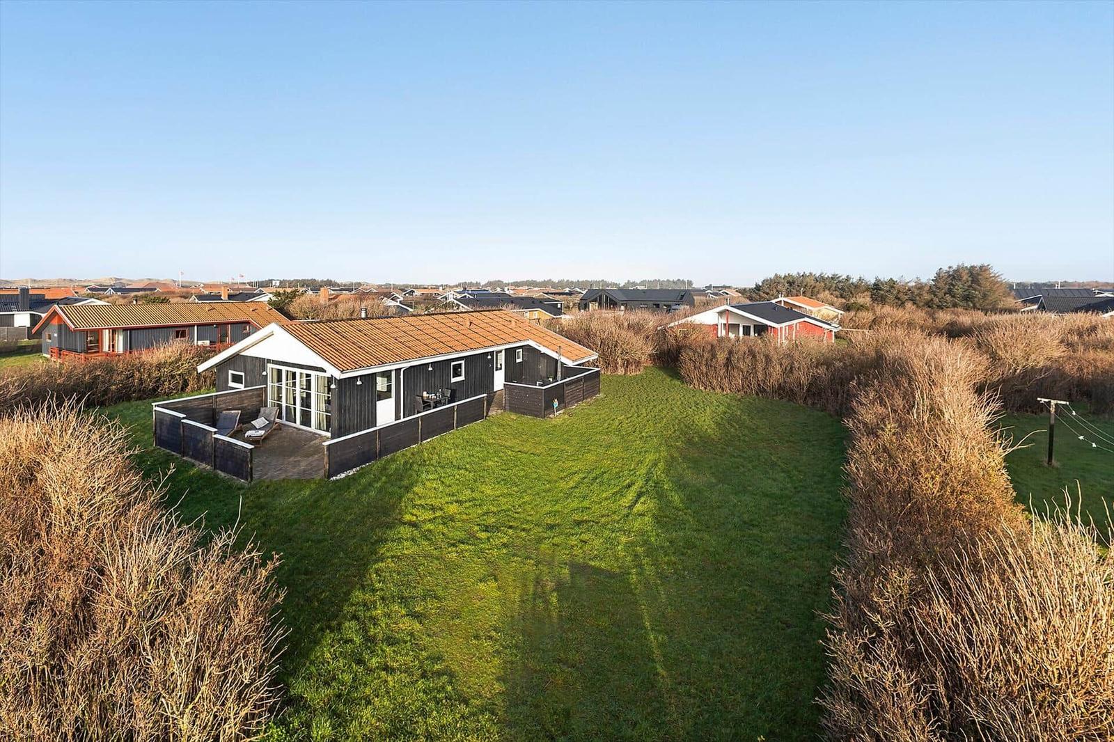 Ein Haus mit Terrasse und Grünfläche. Umgeben von Hecken und weiteren Häusern.