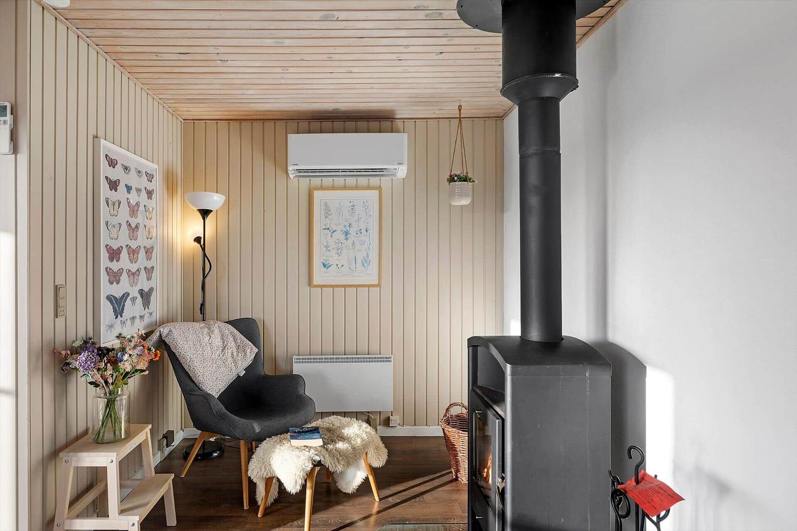 Raum mit Holzwand, Sessel, Kaminofen und Wandbildern.