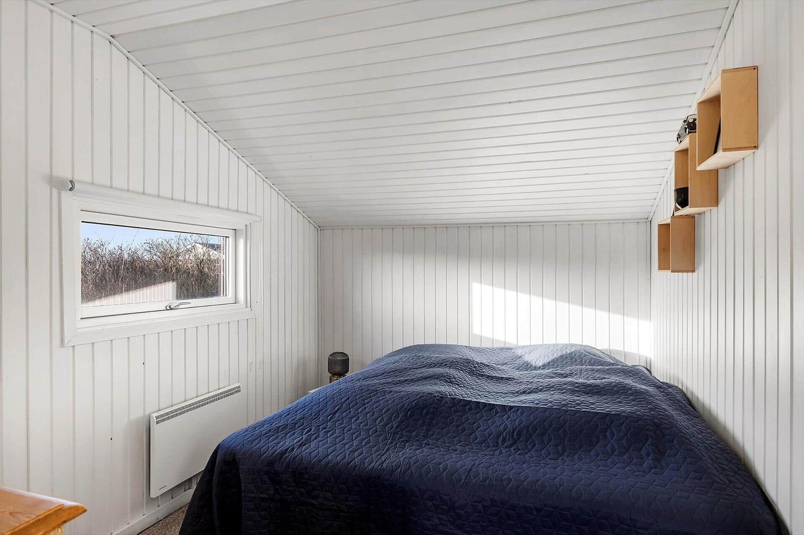 Schlafzimmer mit Bett, Fenster und Wandregalen.