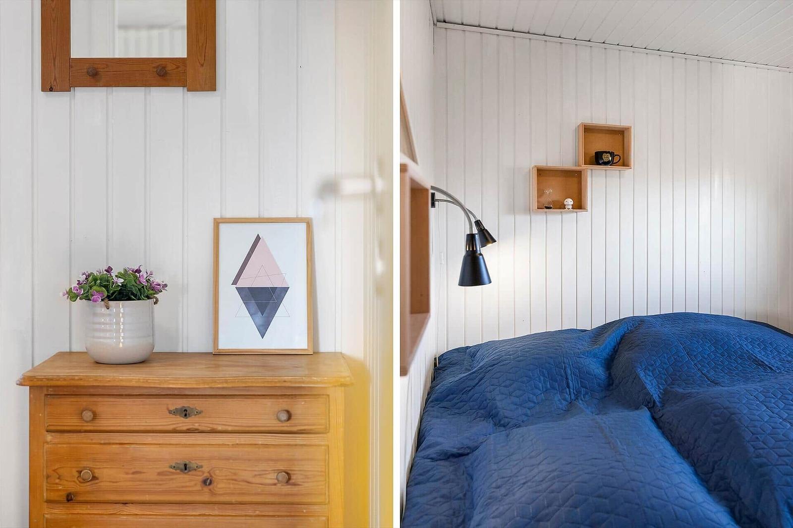 Schlafzimmer mit blauer Bettdecke, Holzkommode und Wandregalen.