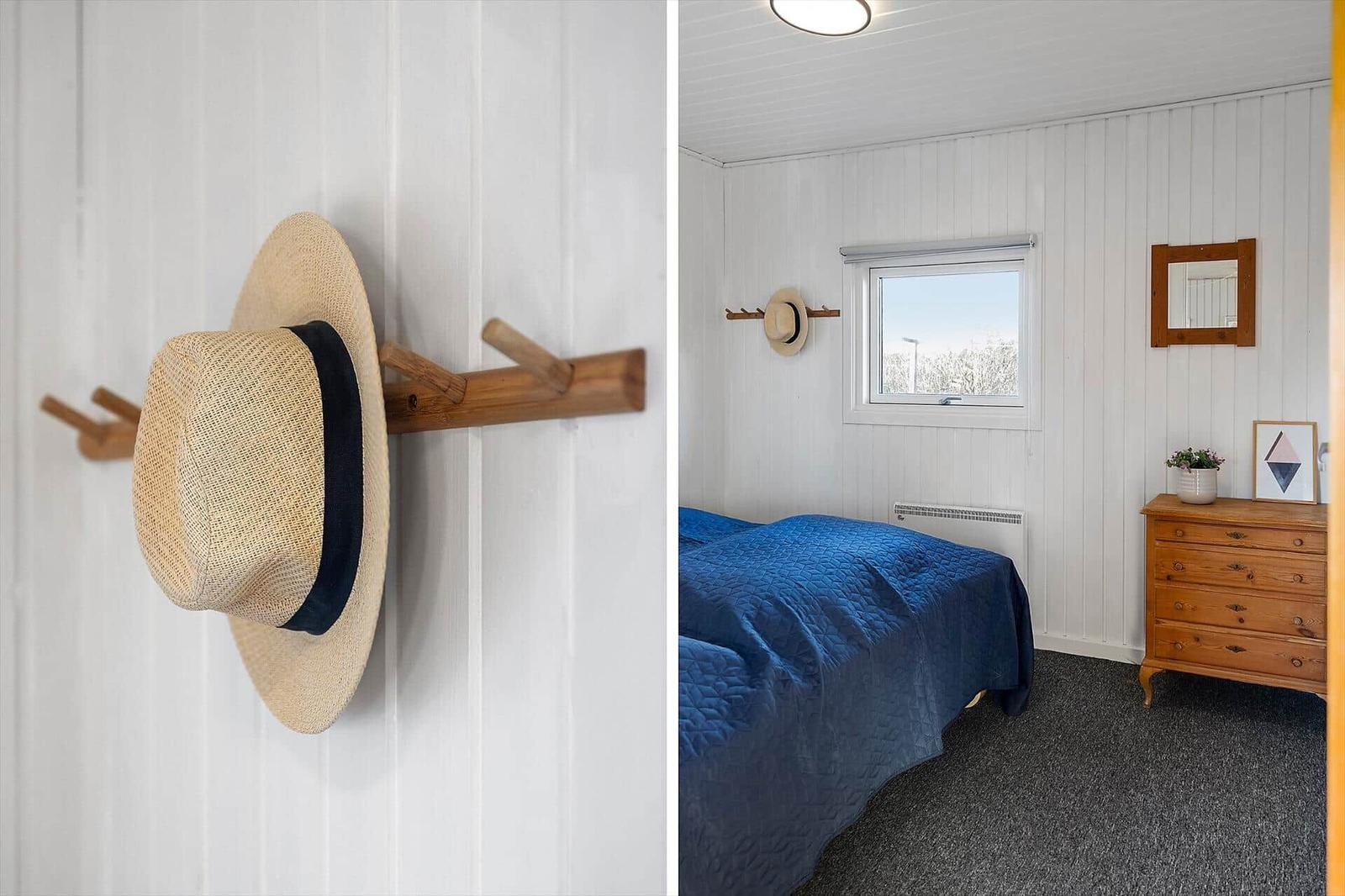Schlafzimmer mit Bett, Kleiderschrank und Fenster. Hut hängt an Wandhalter.