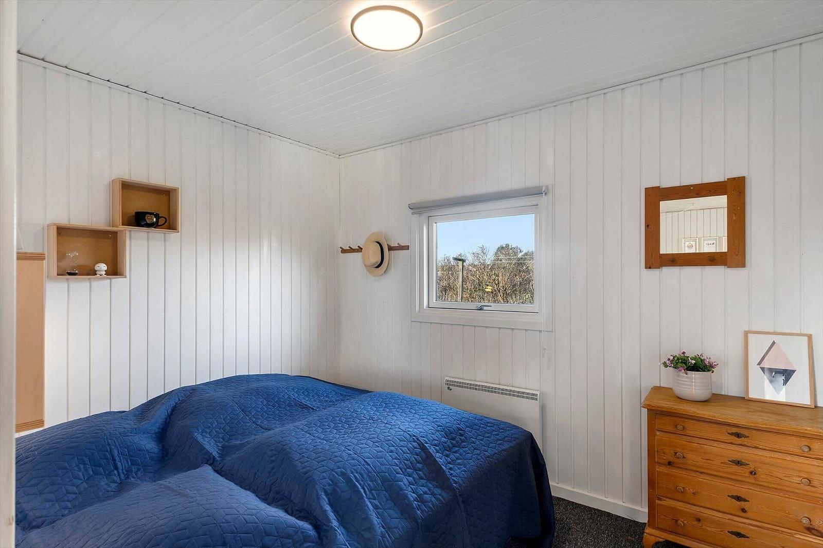 Schlafzimmer mit Bett, Schrank und Fenster. Wände weiß verkleidet.