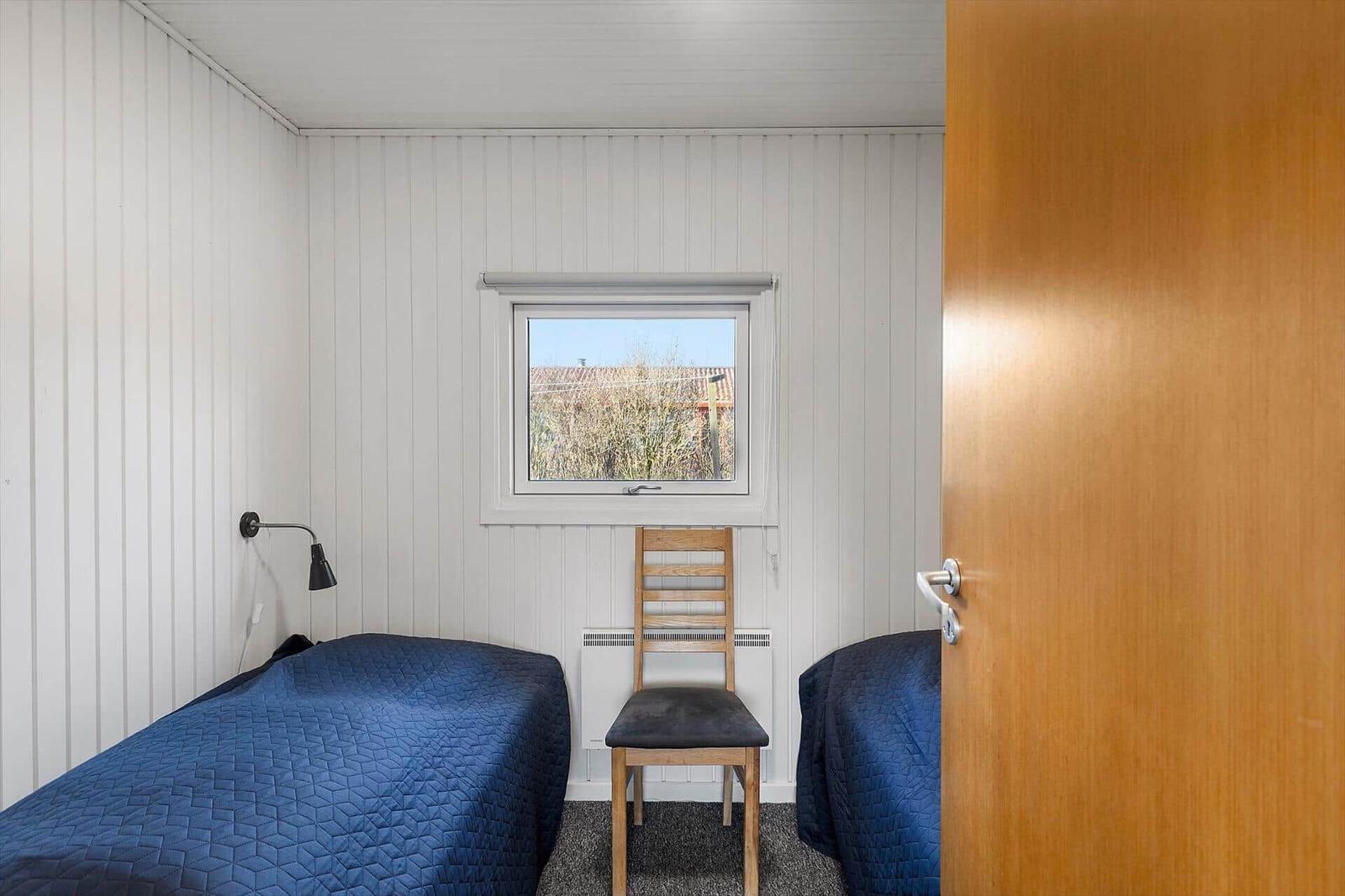 Zimmer mit zwei Betten, Stuhl und Fenster. Wände weiß verkleidet.