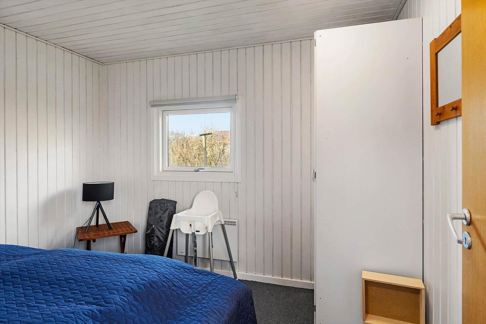 Schlafzimmer mit blauer Bettdecke, Fenster, Hochstuhl und Kleiderschrank.