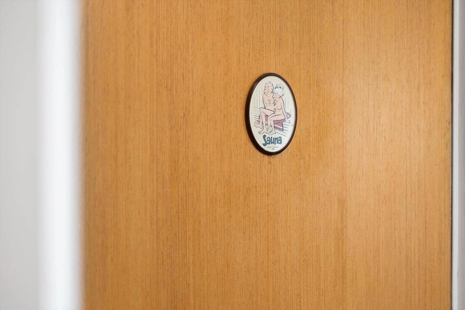 Holztür mit runden Schild, das eine Sauna zeigt.